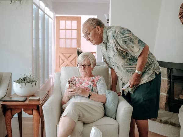 Elderly couple sharing a smartphone, looking at content together in a well-lit living room.